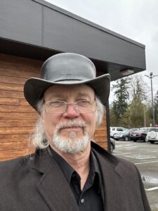 Portrait of Tom with a gray beard and black hat.