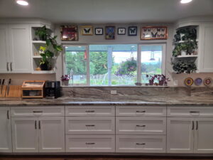 White kitchen cabinets with granite counter below window and shelves.