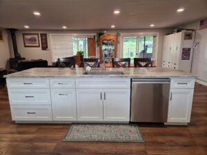 Kitchen island with white cabinets, marble counter, and dishwasher.